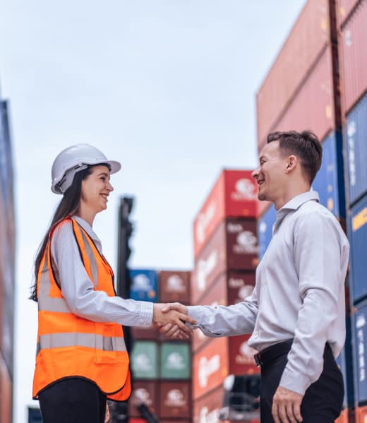 Equipo de R'S WARE dando la mano a cliente internacional junto a contenedores de carga